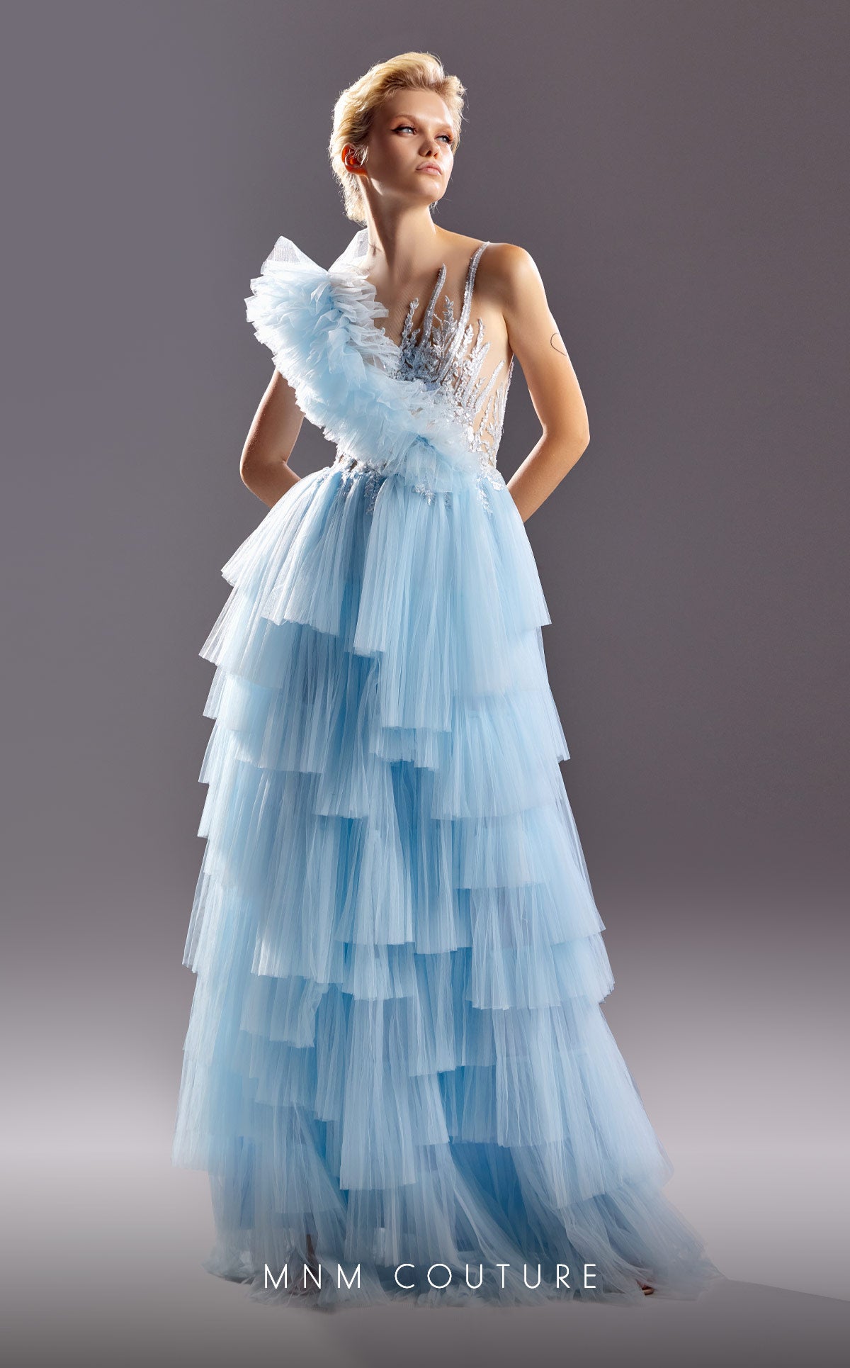 G1528 MNM Couture one shoulder blue tiered long dress boasts a sheer bodice with intricate beaded detailing crawling upwards creating an incredible flattering pattern for your figure